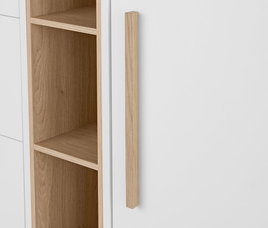 Detail bílé komody »Eklund« se zásuvkami a dvířky, s dřevěnou rukojetí a otevřenými policemi.