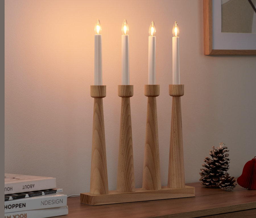 Čtyři LED svíčky ve dřevěném svícnu stojí na skříňce.