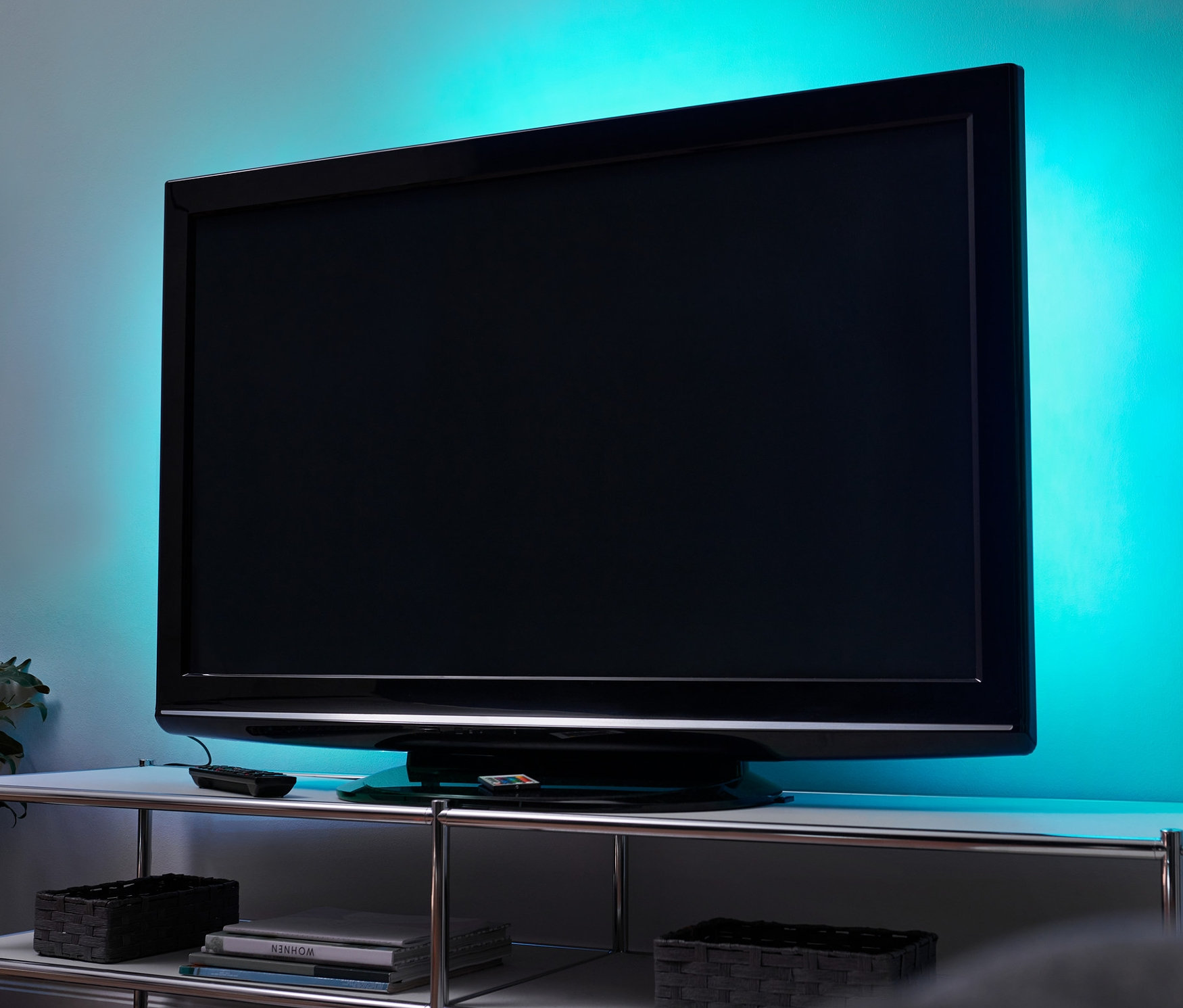 Televize s LED podsvícením pro TV, umístěná na bílém stolku. V pozadí je rostlina.