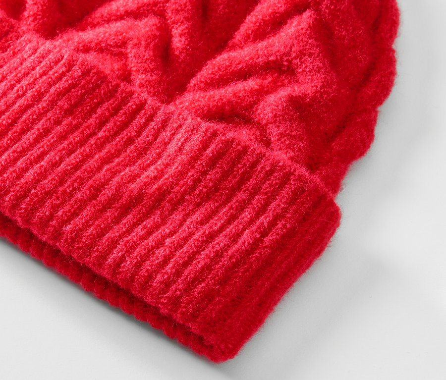Detail červené pletené čepice s copánkovým vzorem.