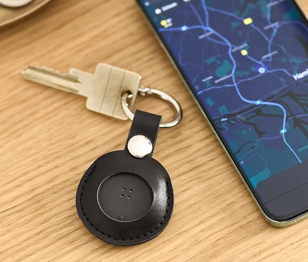 Na stole leží klíče s černým chytrým lokátorem s přívěskem a mobilní telefon s mapou.
