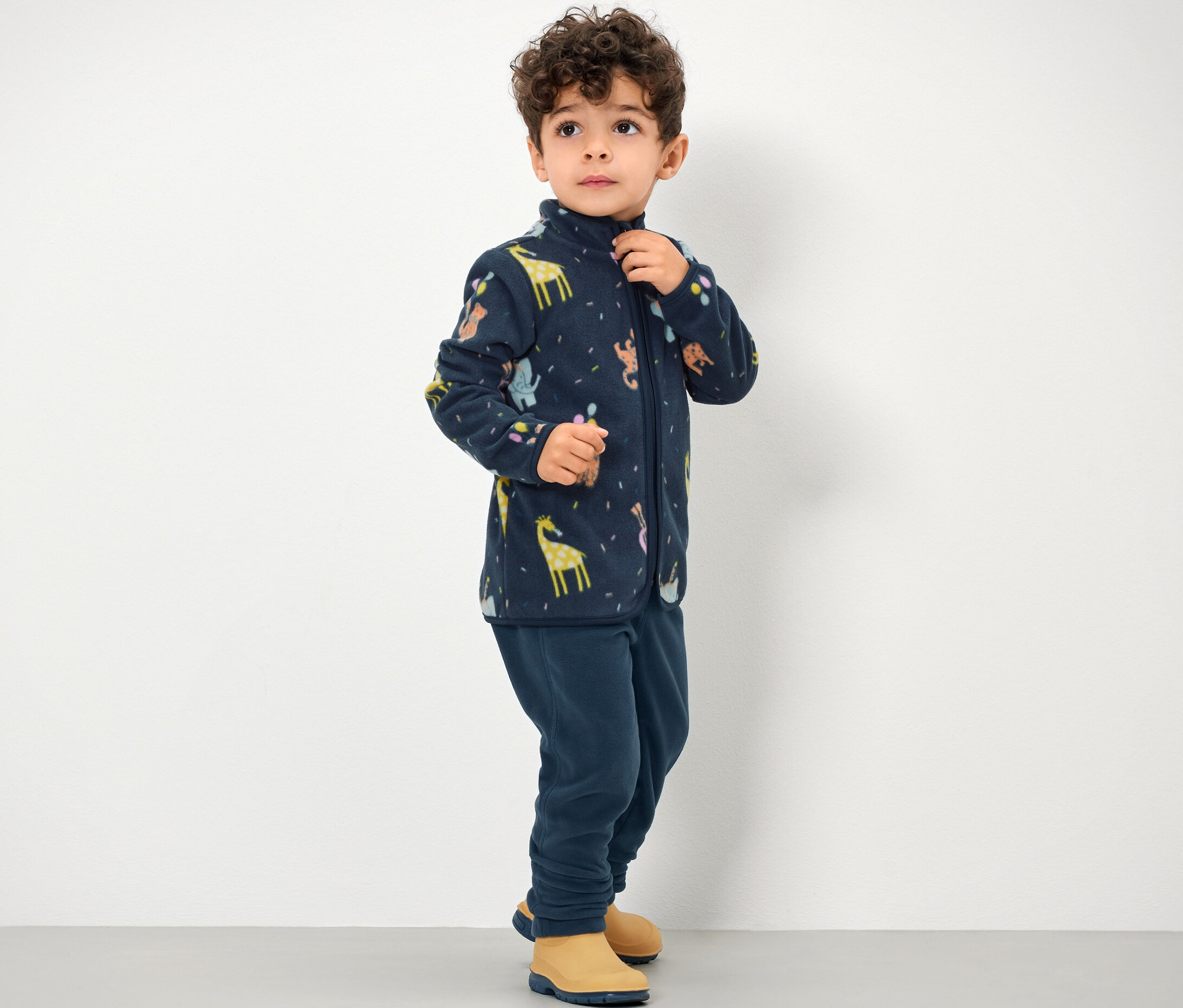 Chlapec má na sobě dětské fleecové kalhoty a bundu se zipem a zvířecím potiskem.