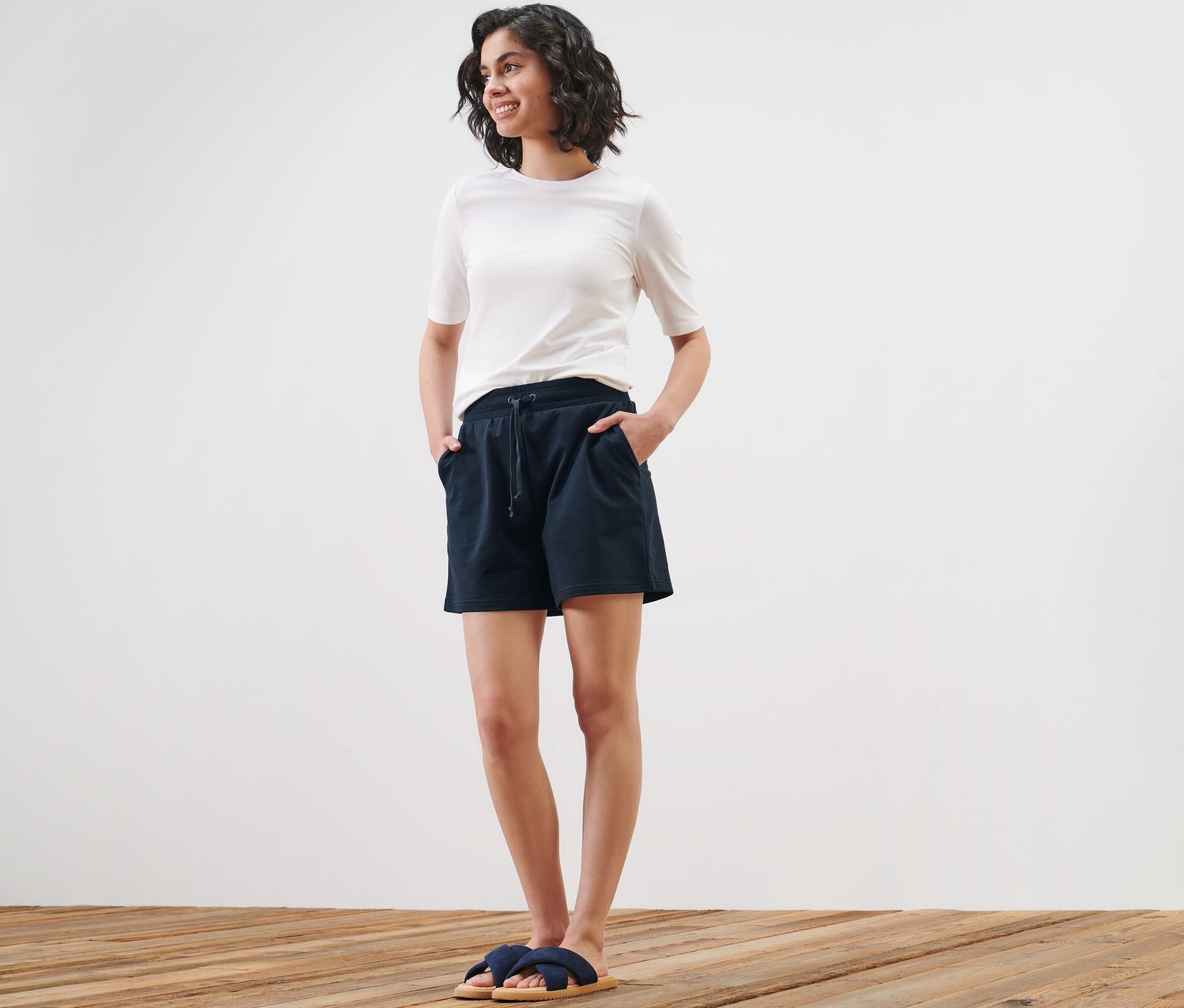 Žena pózuje v teplákových šortkách a tričku.