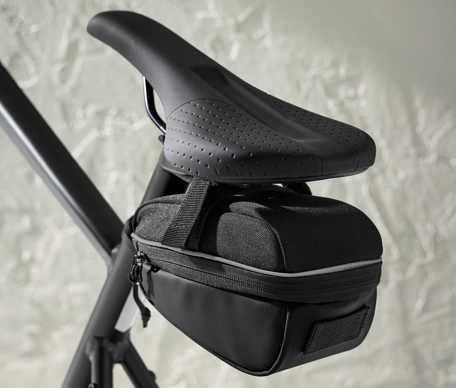 Černá cyklistická brašna pod sedlem připevněná k sedlu kola.