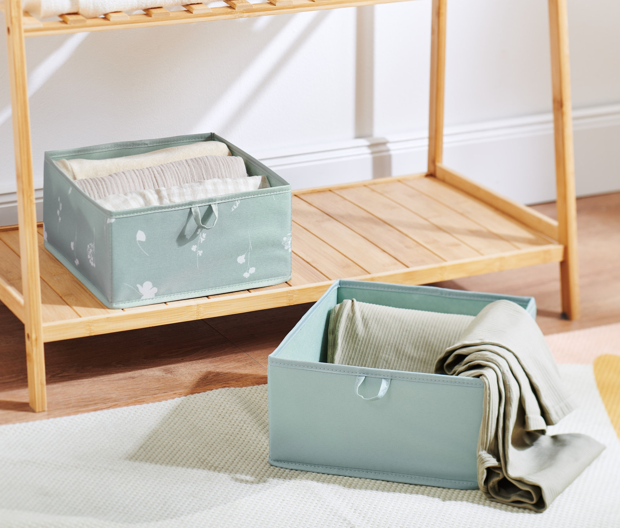 Dva velké úložné boxy do zásuvky stojí na dřevěném regálu a koberci.