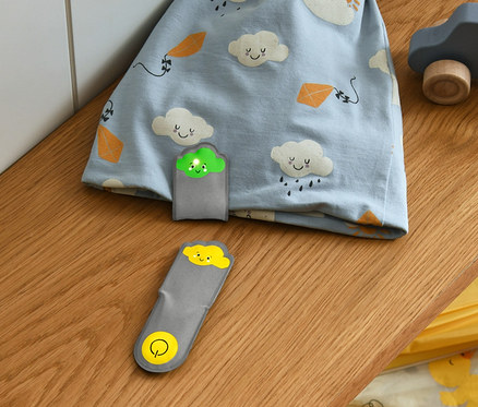 Modrá čepice s potiskem mraků a 2 magnetická LED světýlka mráčky leží na polici.