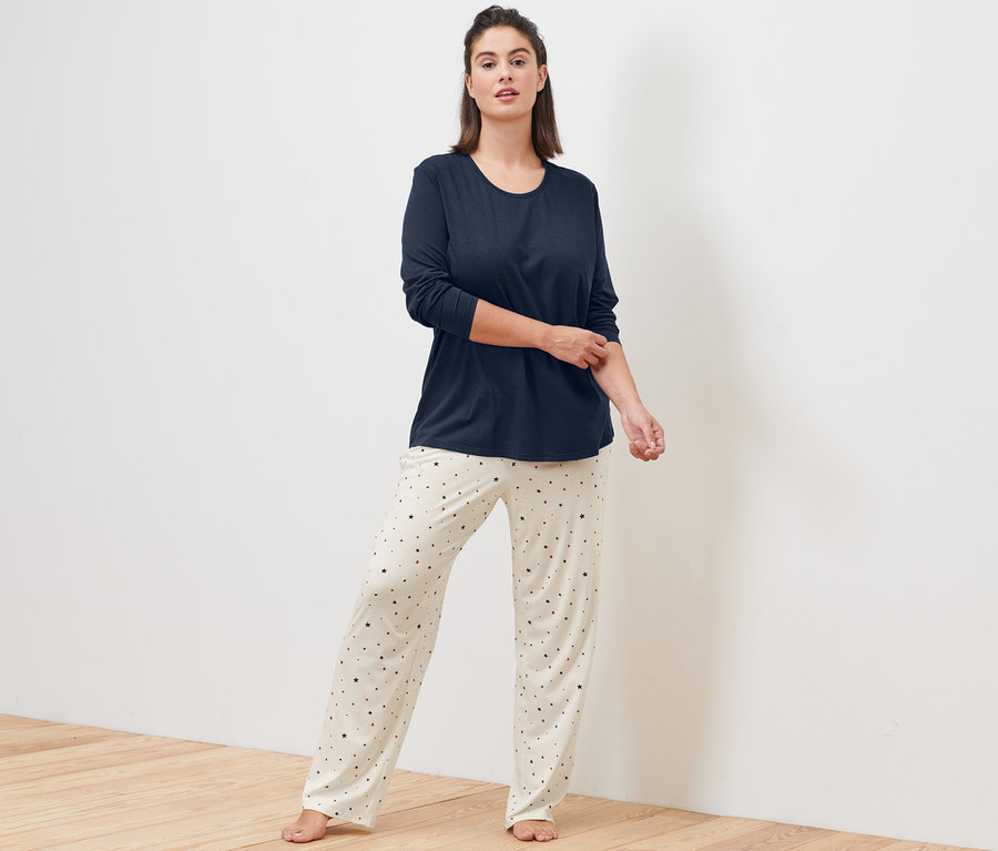 Žena stojí a má na sobě krémové pyžamo.