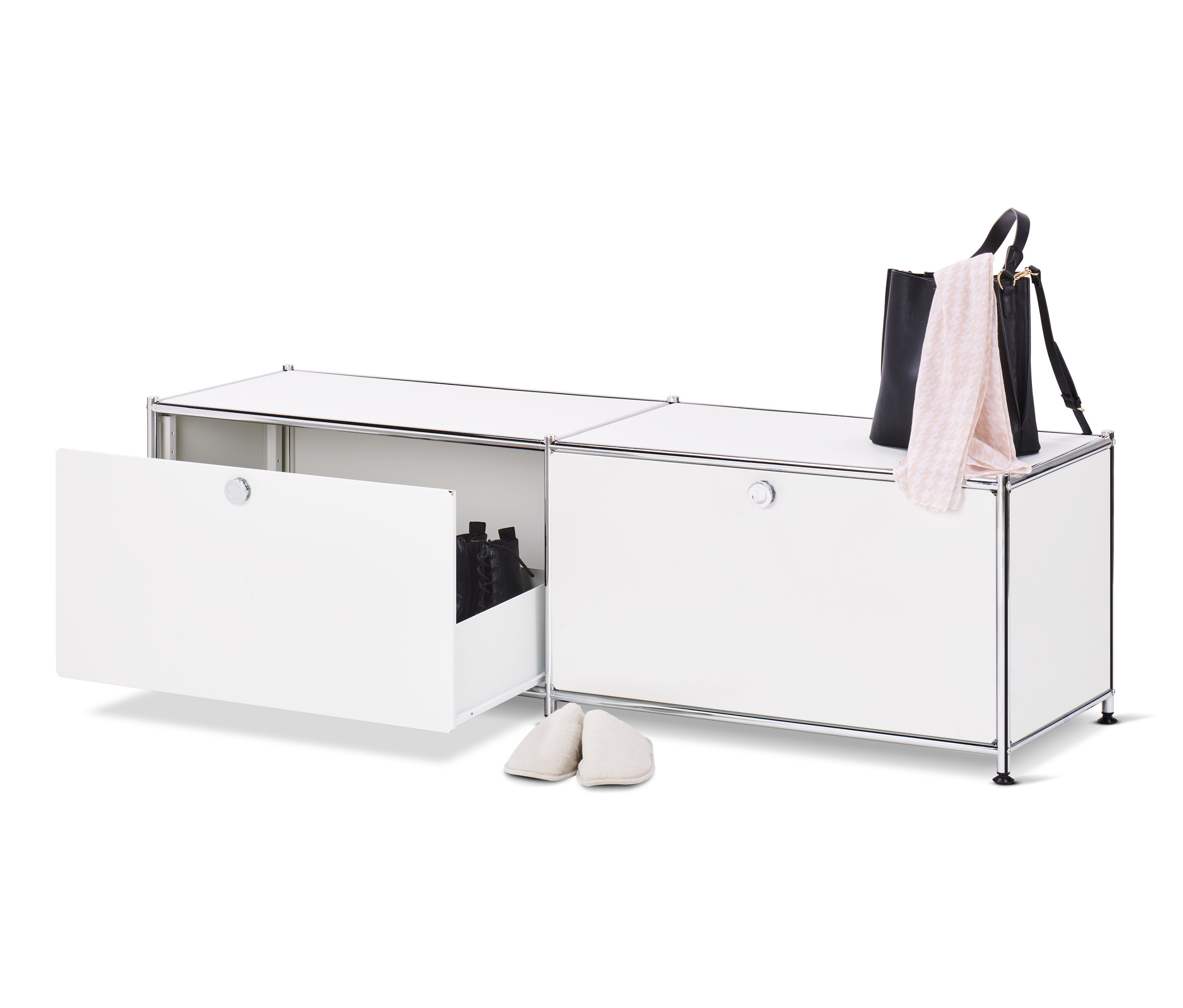 Otevřená bílá kovová nízká skříňka CN3 se zásuvkami a botami uvnitř, vedle ní stojí pár krémových pantoflí, na horní straně skříňky leží černá kabelka a růžový šátek.