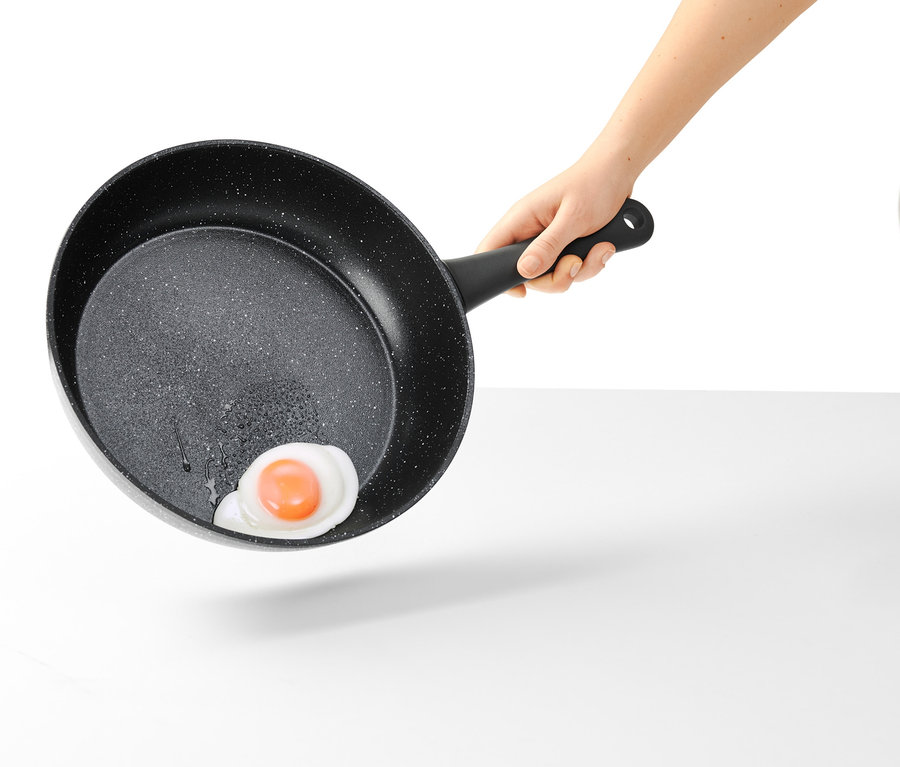Ruka drží 28cm profi pánev v kamenném vzhledu s smaženým vejcem.