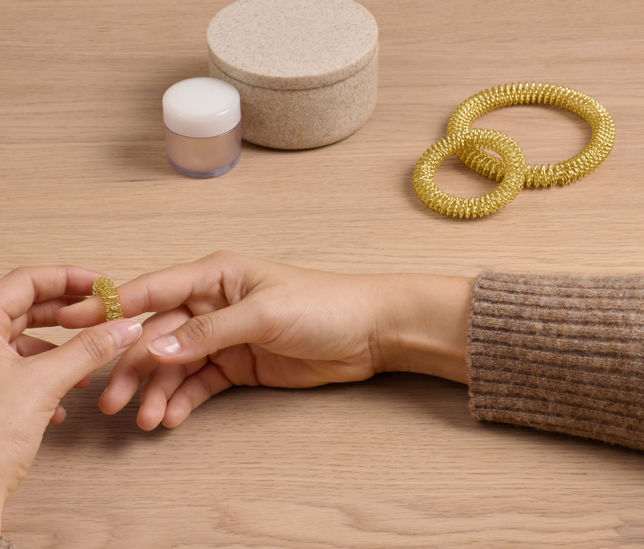 Žena si navléká na prst zlatý akupresurní kroužek ze sady. Na stole leží další dva kroužky a krabička.