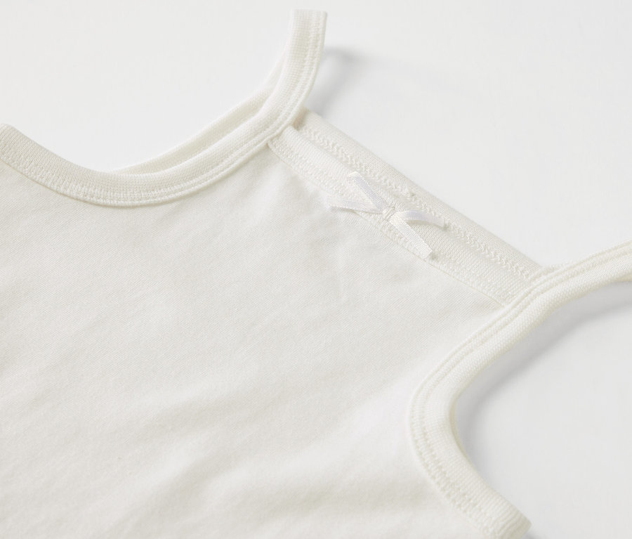 Detail bílého kojeneckého body s ramínky a mašličkou.