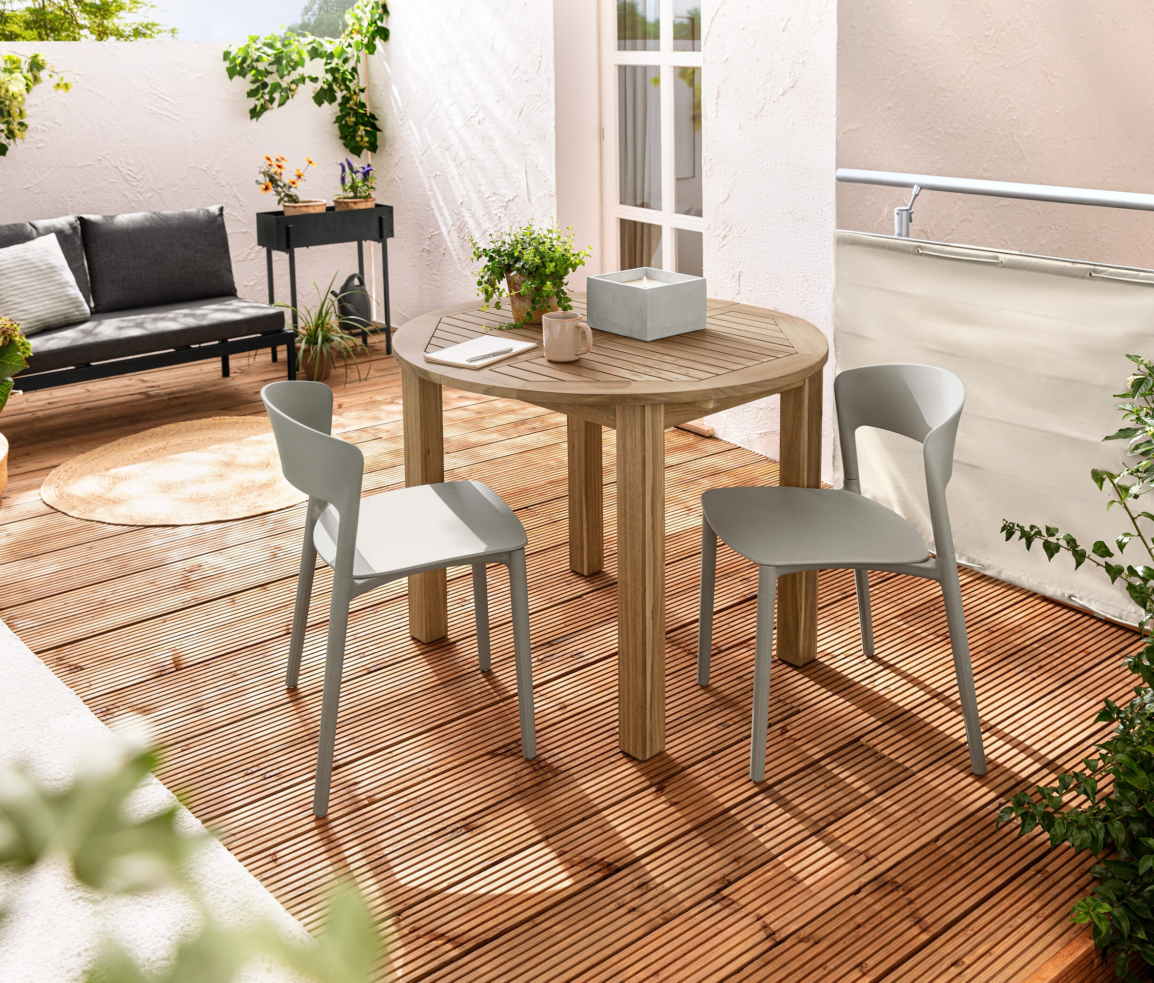 Dva plastové židle stojí u kulatého rozkládacího stolu na balkóně. Na stole je svíce XL z pravého vosku s LED v betonové nádobě. Balkónová zástěna a ochrana proti větru, krémová, je vidět v pozadí.