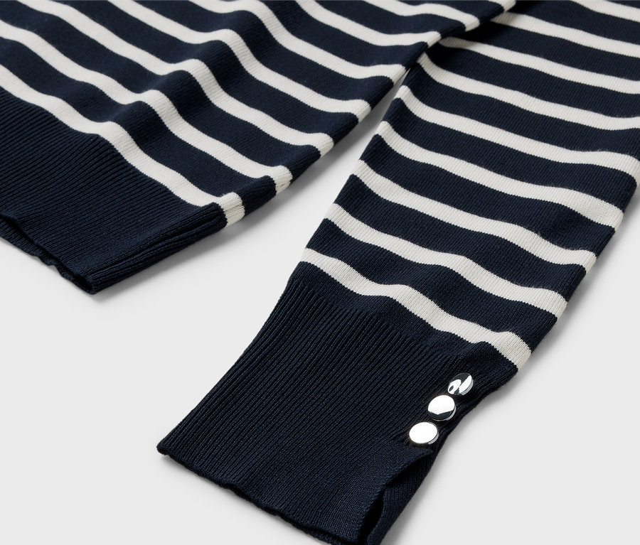 Detail pruhovaného svetru s dlouhým rukávem a stříbrnými knoflíky na manžetě.