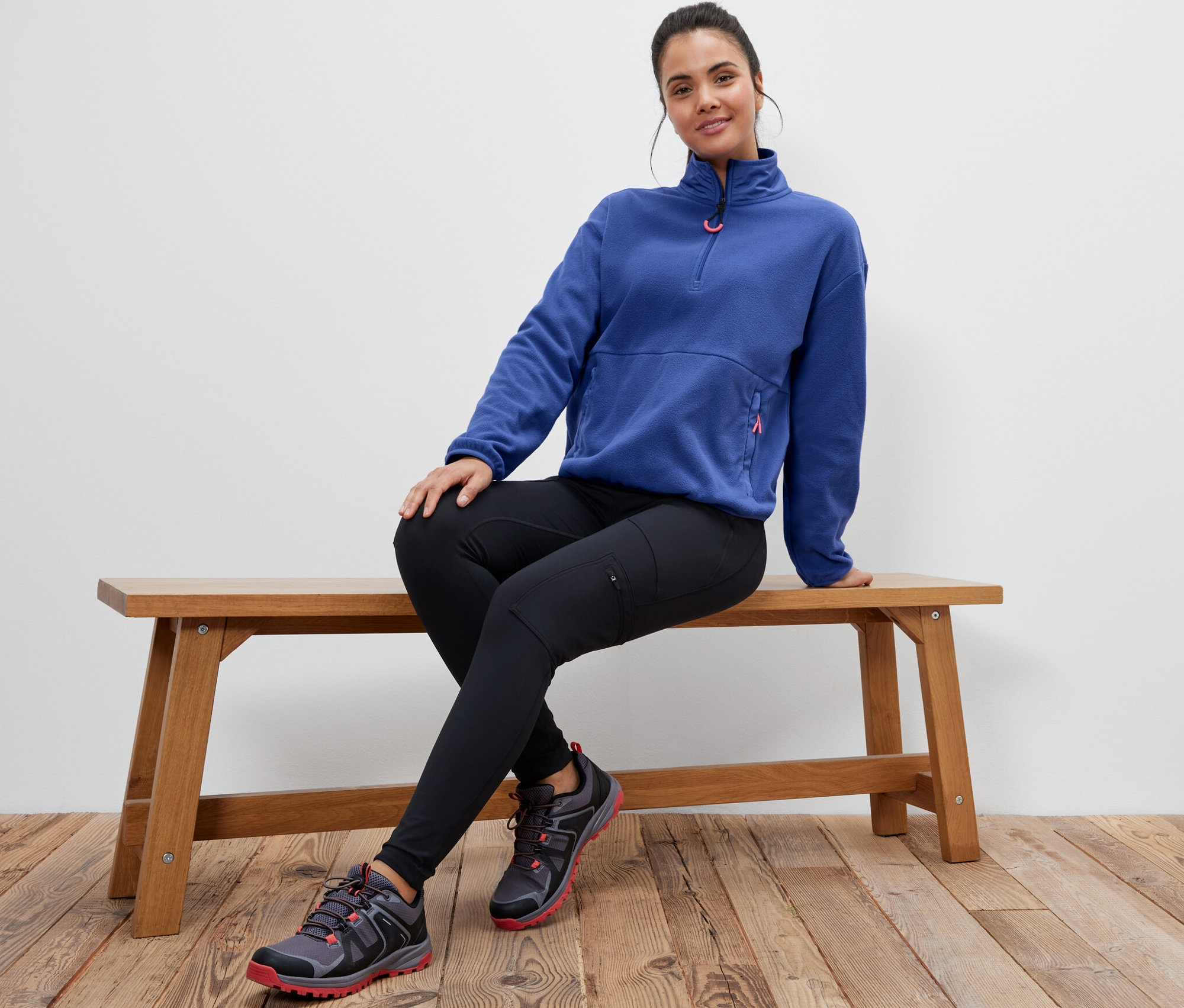 Žena sedí na lavici a má na sobě modrou fleecovou mikinu.