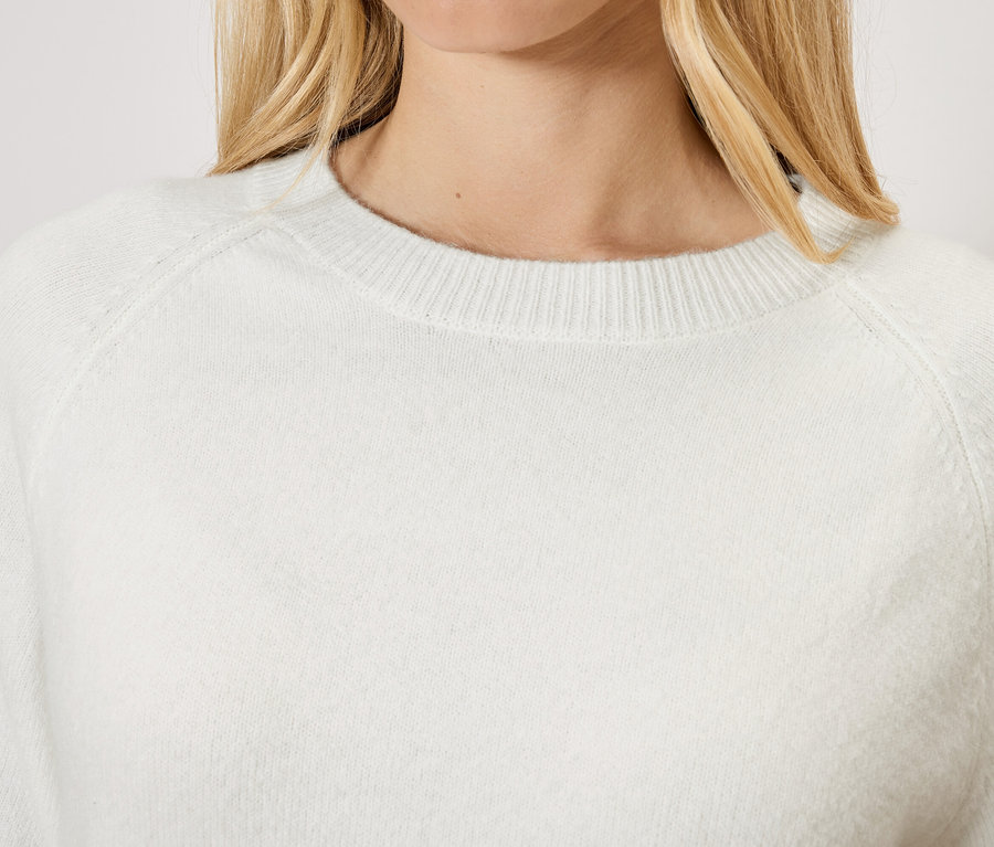 Žena s blond vlasy má na sobě bílý svetr.