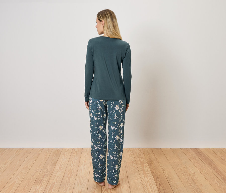 Žena stojí zády, má na sobě zelené pyžamo s dlouhým rukávem a květinové kalhoty.