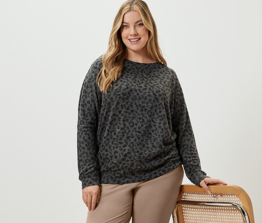 Žena pózuje v béžových teplákových kalhotách a tričku s netopýřími rukávy.