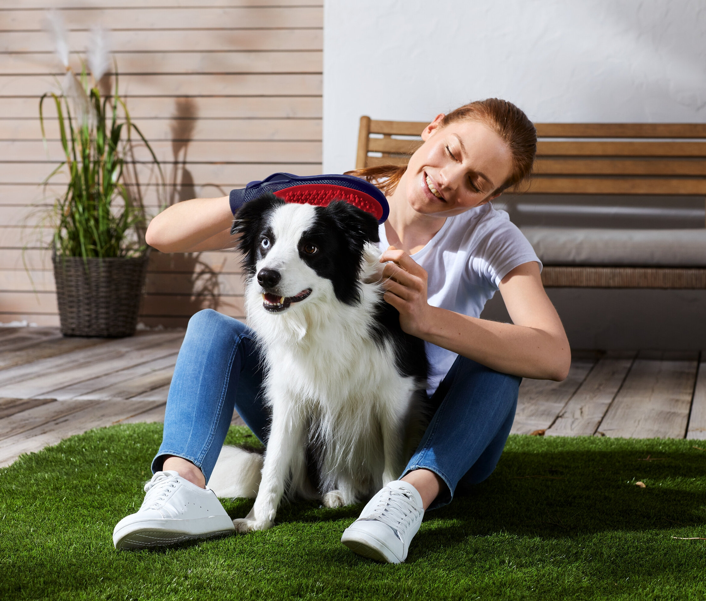 Žena sedí na trávě a kartáčuje psa s černobílým zbarvením.