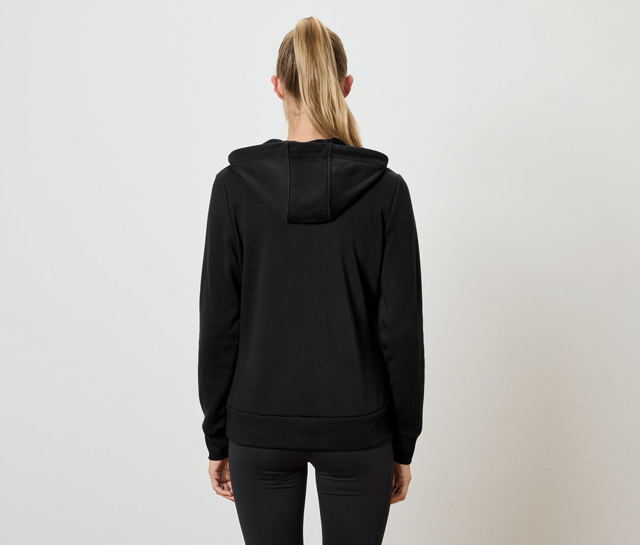 Zezadu je vidět žena s blond vlasy v culíku, oblečená v černé mikině s kapucí a černých kalhotách.