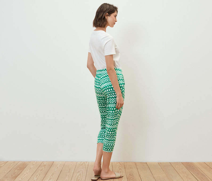 Žena stojí bokem a má na sobě bílé tričko a 3/4 žerzejové kalhoty s potiskem.