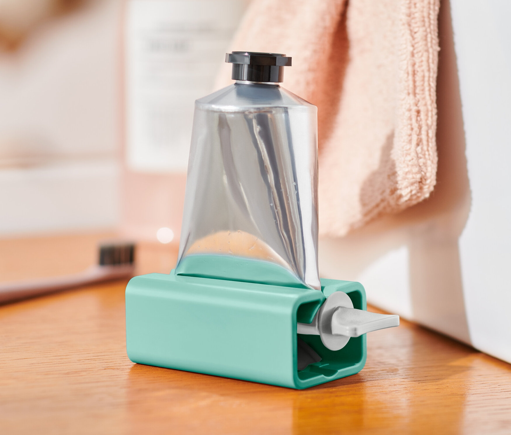 Stříbrná tuba v tyrkysovém vytlačovači tub na dřevěné skříňce.