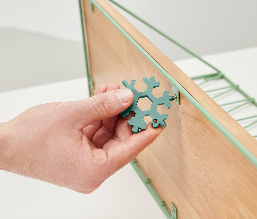 Ruka drží multifunkční klíč a utahuje šroub na dřevěné polici.