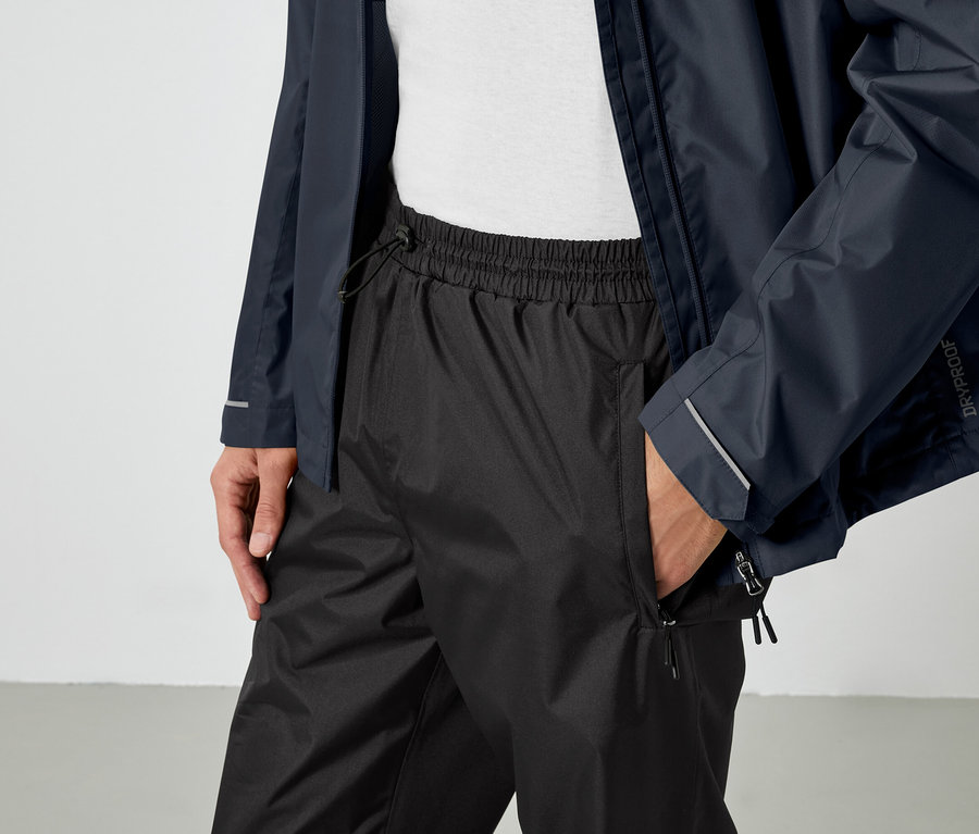 Muž má ruku v kapse černých kalhot a na sobě modrou bundu.