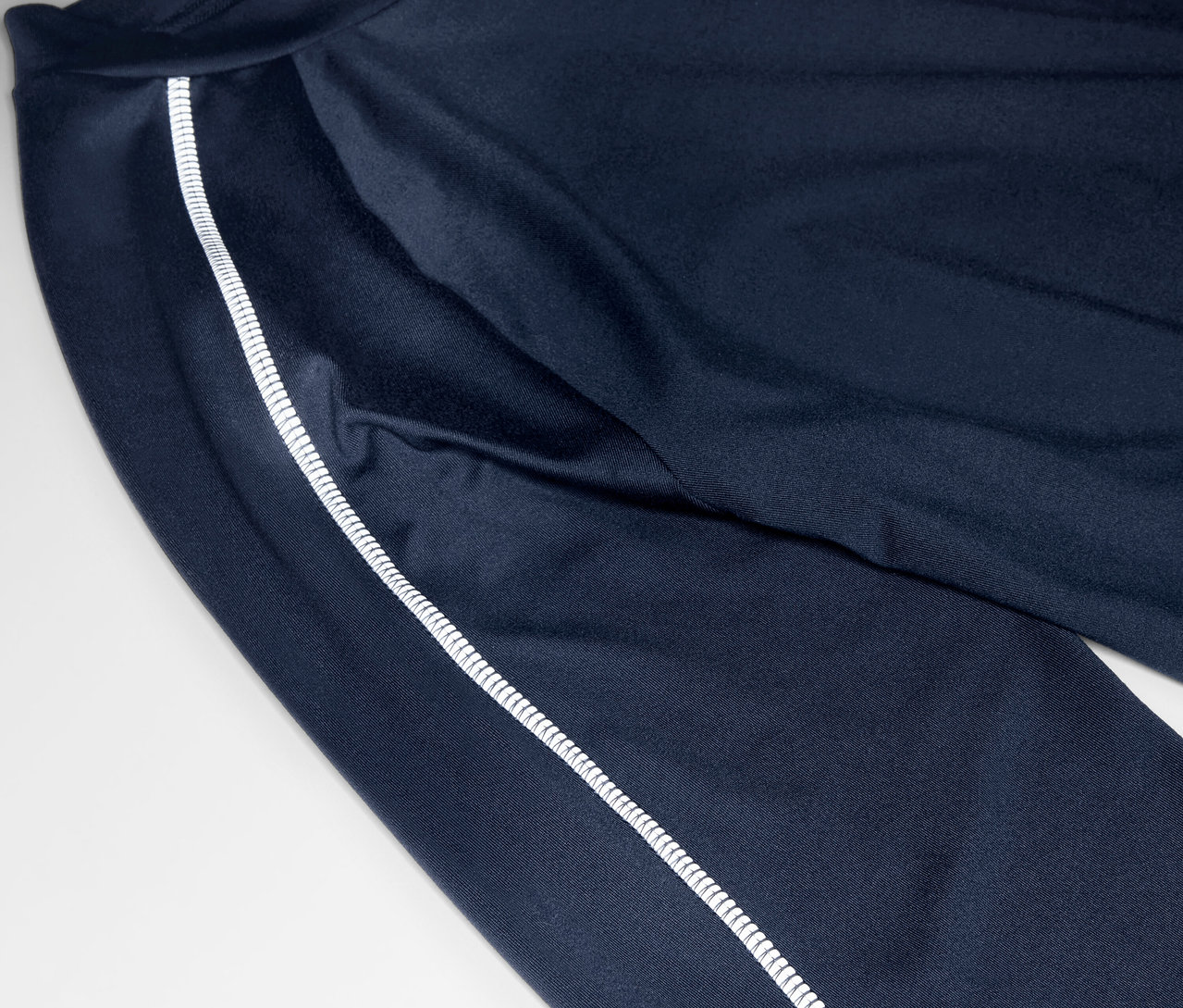 Detailní záběr na tmavě modré tepláky s bílým pruhem na boku.