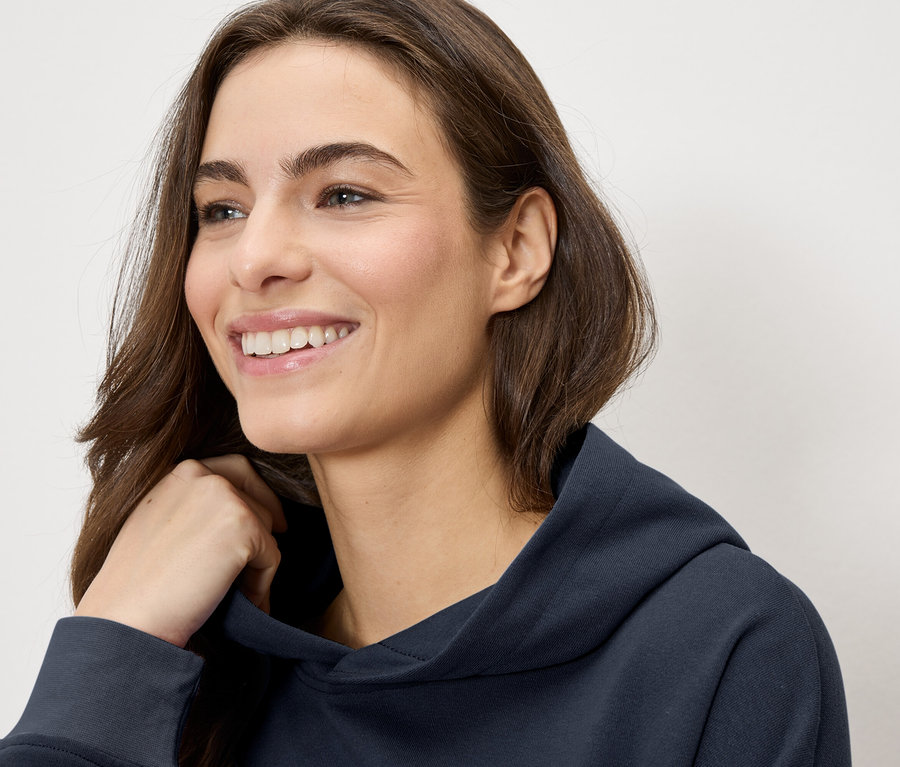 Usmívající se žena v tmavě modré mikině s kapucí.