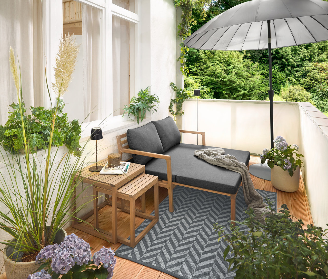 Zařízení na balkóně s rozkládací zahradní pohovkou, venkovním kobercem (cca 165 x 115 cm), balkónovou zástěnou a ochranou proti větru v krémové barvě, venkovní dobíjecí stolní lampou LED v černé barvě a venkovní dobíjecí stojací lampou LED v černé barvě.