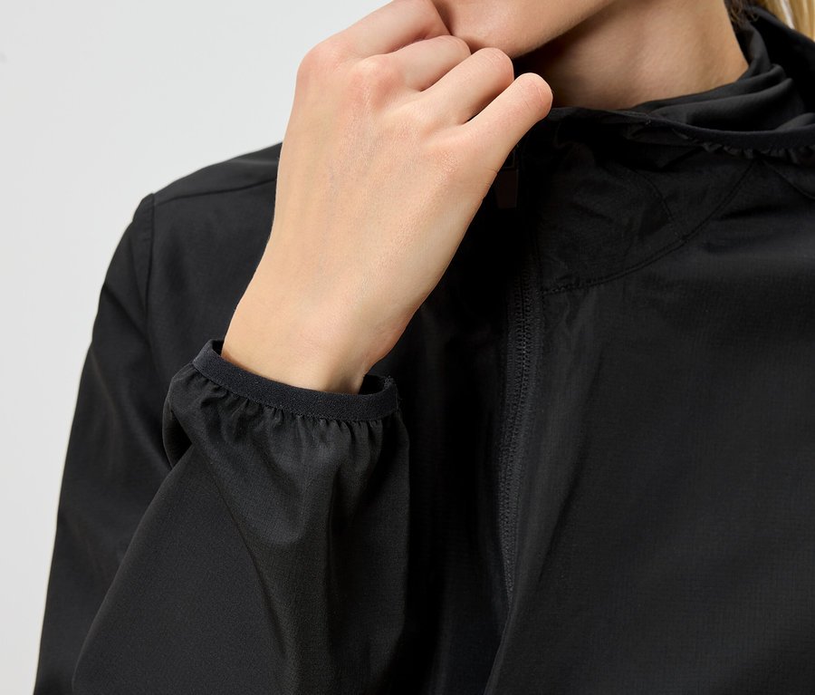 Detail osoby v černé pláštěnce s kapucí, která si zapíná zip.