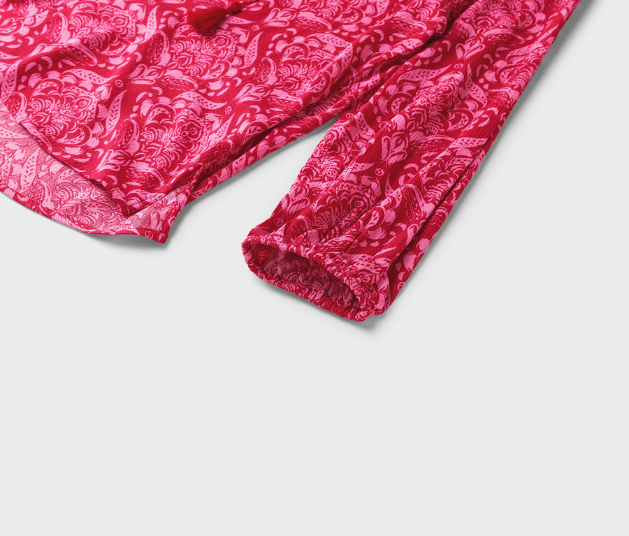 Detail červené halenky s růžovým květinovým vzorem a dlouhými rukávy.