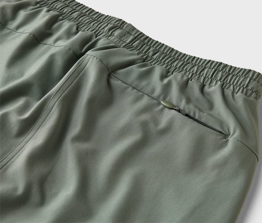 Detail olivově zelených kalhot s elastickým pasem a kapsou na zip.