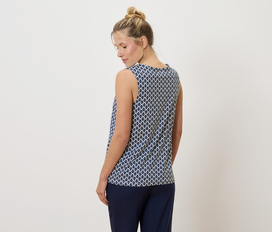 Blonďatá žena s drdolem má na sobě modrobílé tílko a tmavě modré kalhoty, pohled zezadu.