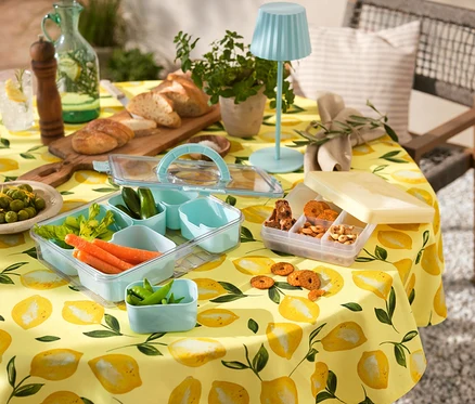 Žlutý ubrus s citrony, Snacktray To-Go se zeleninou a sušenkami, malá LED lampička, chléb, nápoje a olivy.
