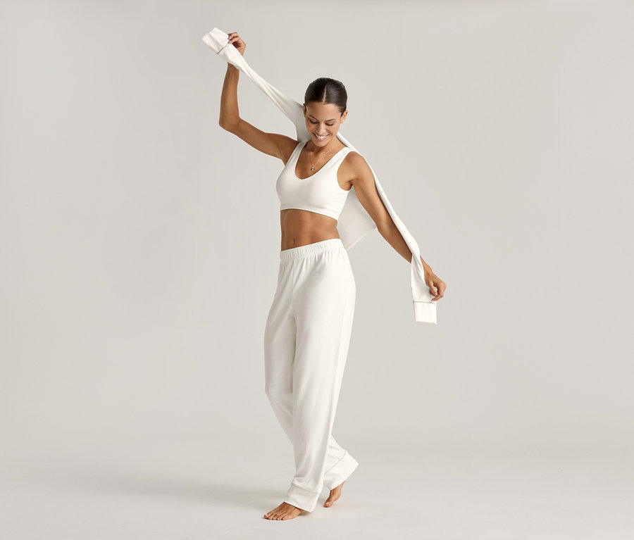 Žena v pyžamové soupravě a krémové bezešvé podprsence drží horní díl.