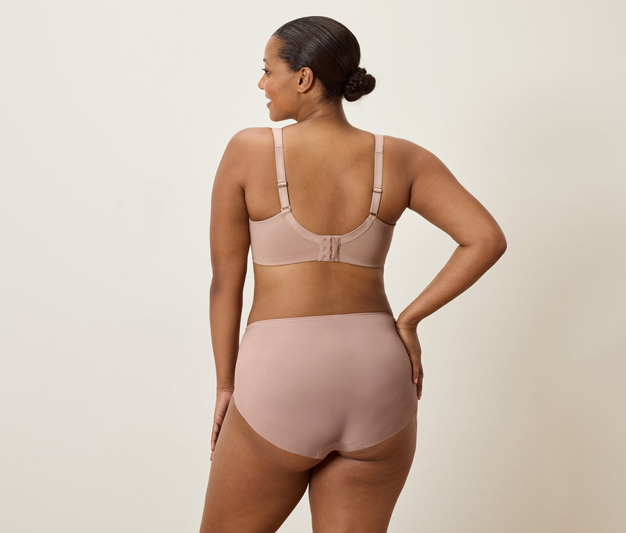 Žena zezadu, má na sobě tělovou podprsenku a kalhotky, s jednou rukou na boku.