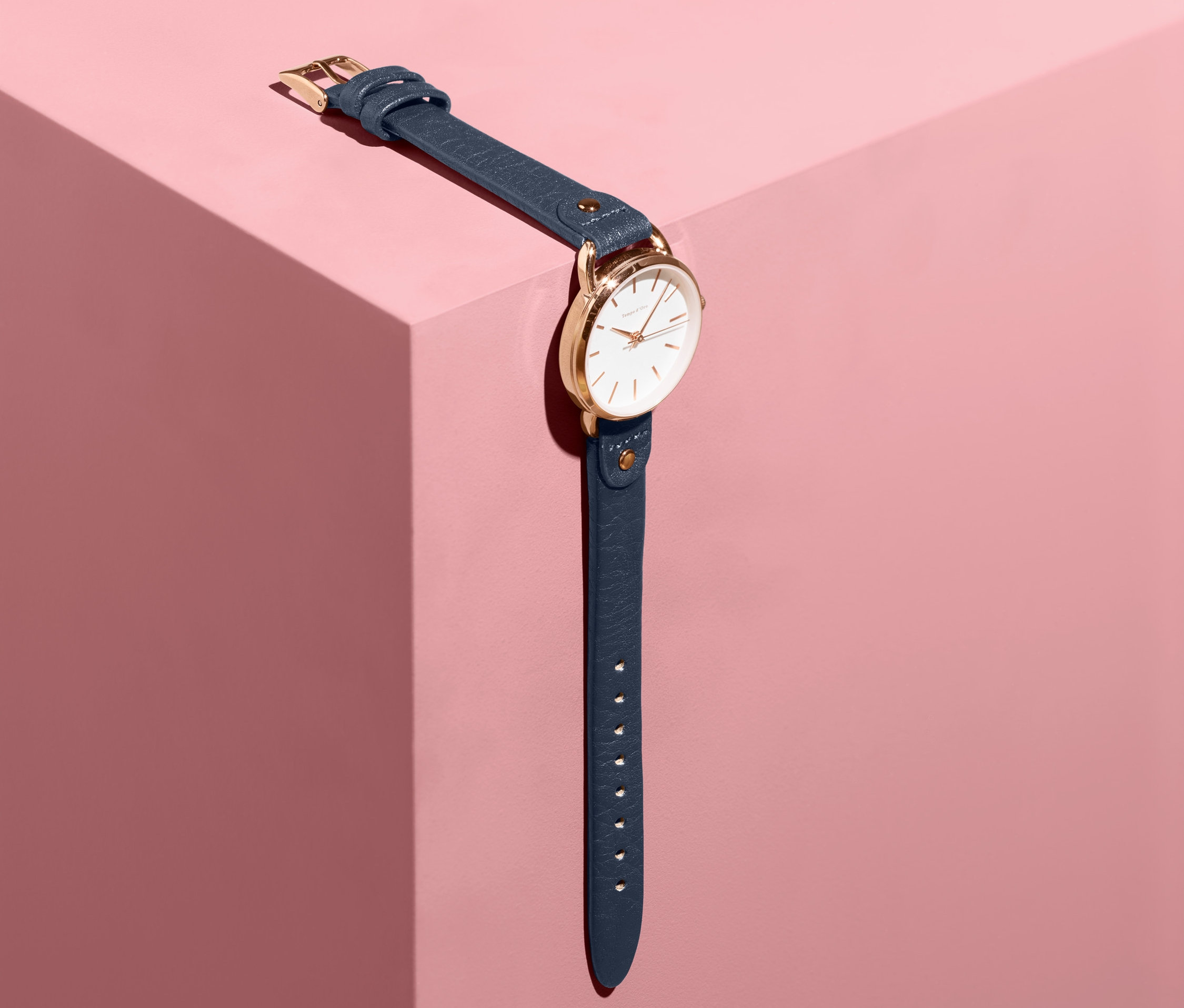 Dámské hodinky s koženým řemínkem leží na růžovém podstavci.