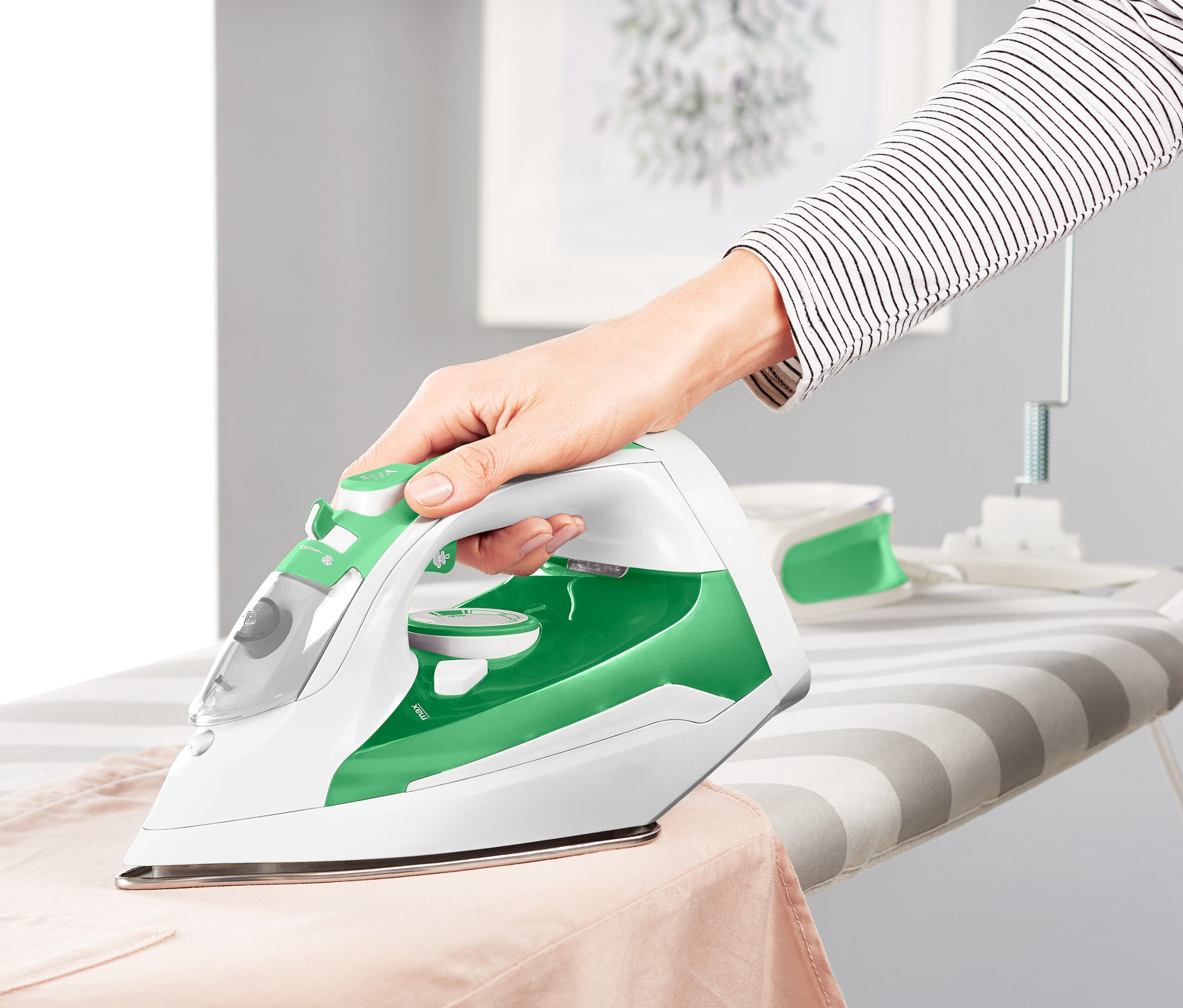 Žena žehlí bezkabelovou napařovací žehličkou na žehlicím prkně.