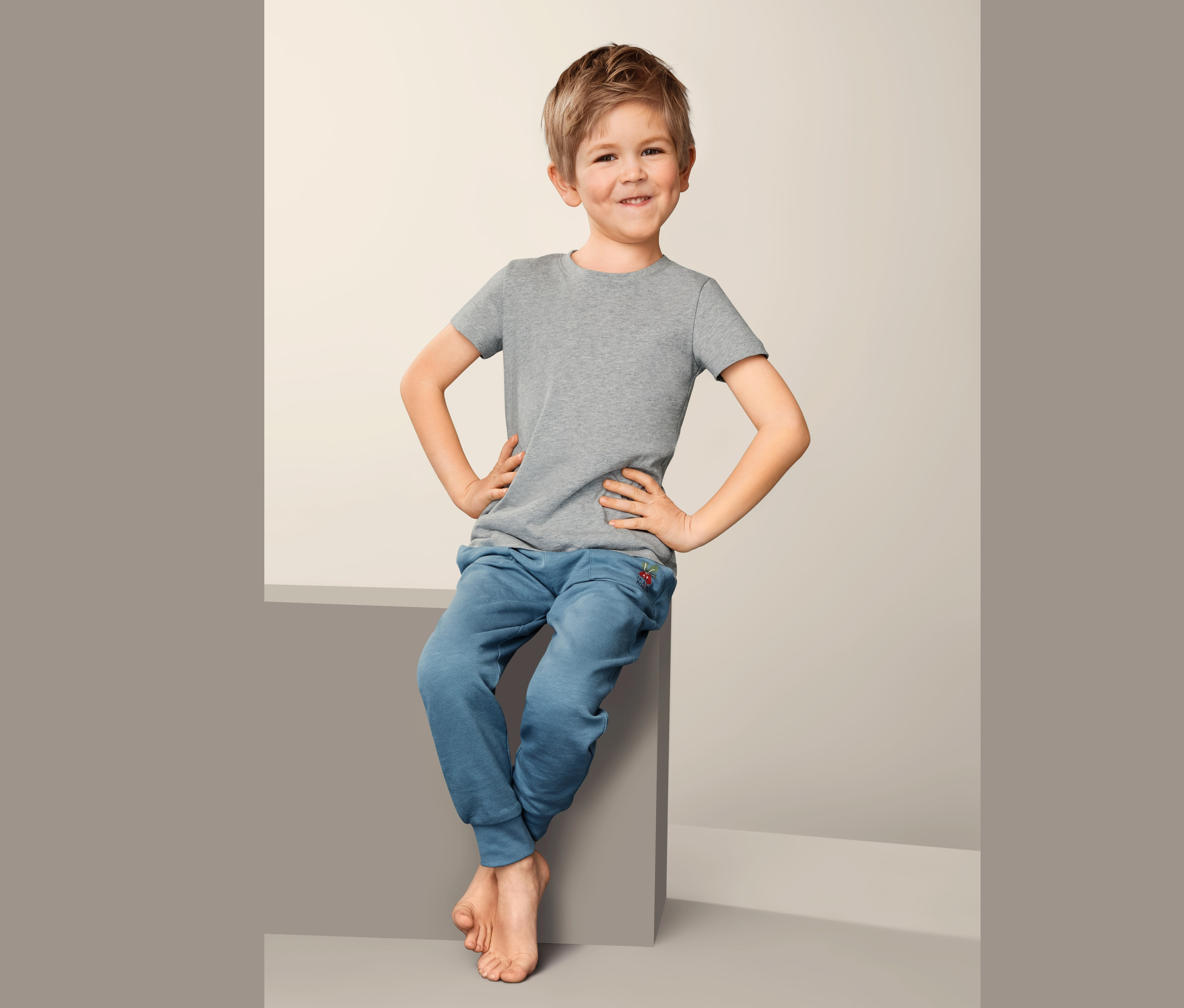 Chlapec sedí a má na sobě šedé spodní tričko (2 ks) a modré tepláky.