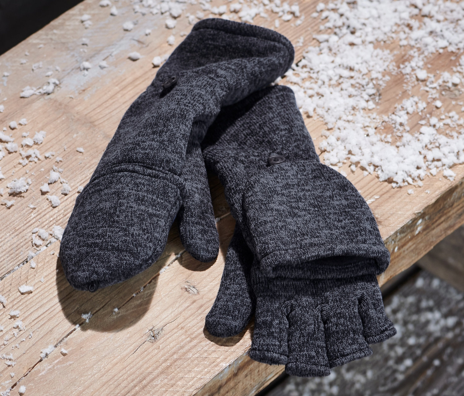 Modré odklápěcí palčáky z pleteného fleecu leží na dřevěné lavici vedle plátěného batohu.