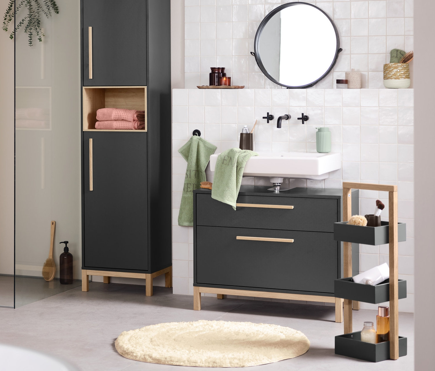 Interiér koupelny s umyvadlem, zrcadlem a úložnými skříňkami Eklund v antracitové barvě. V popředí je vana.