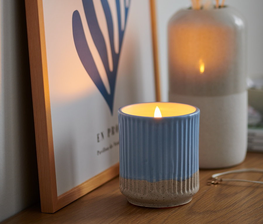 Modrá LED svíčka z pravého vosku stojí na dřevěné polici vedle obrázku.