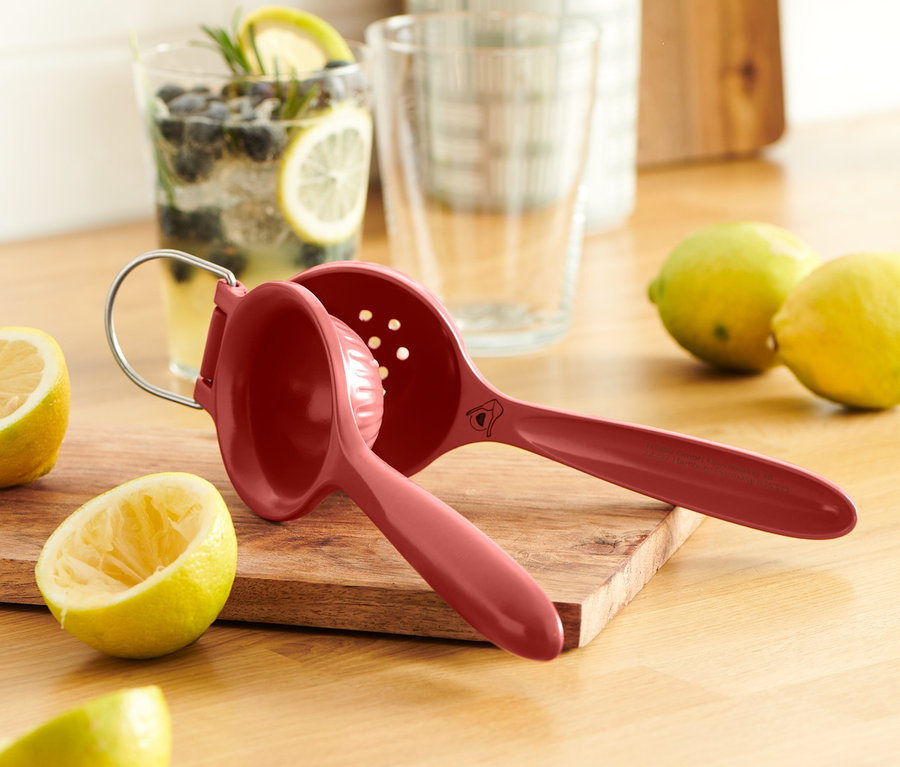 Červený lis na citrusy na dřevěném prkénku vedle citronů.