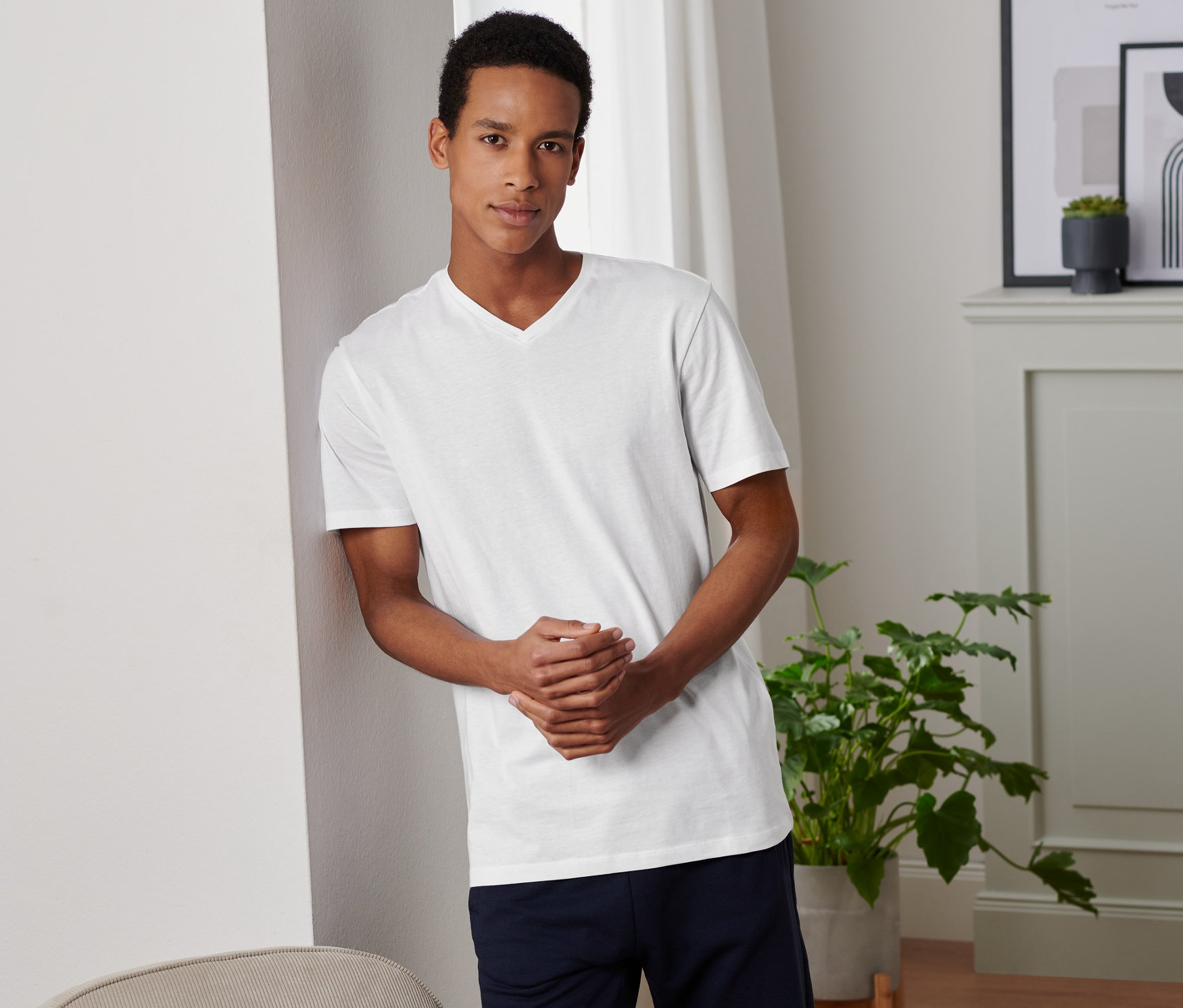 Muž opřený o zeď má na sobě bílé tričko s výstřihem do V z dvoukusové sady.