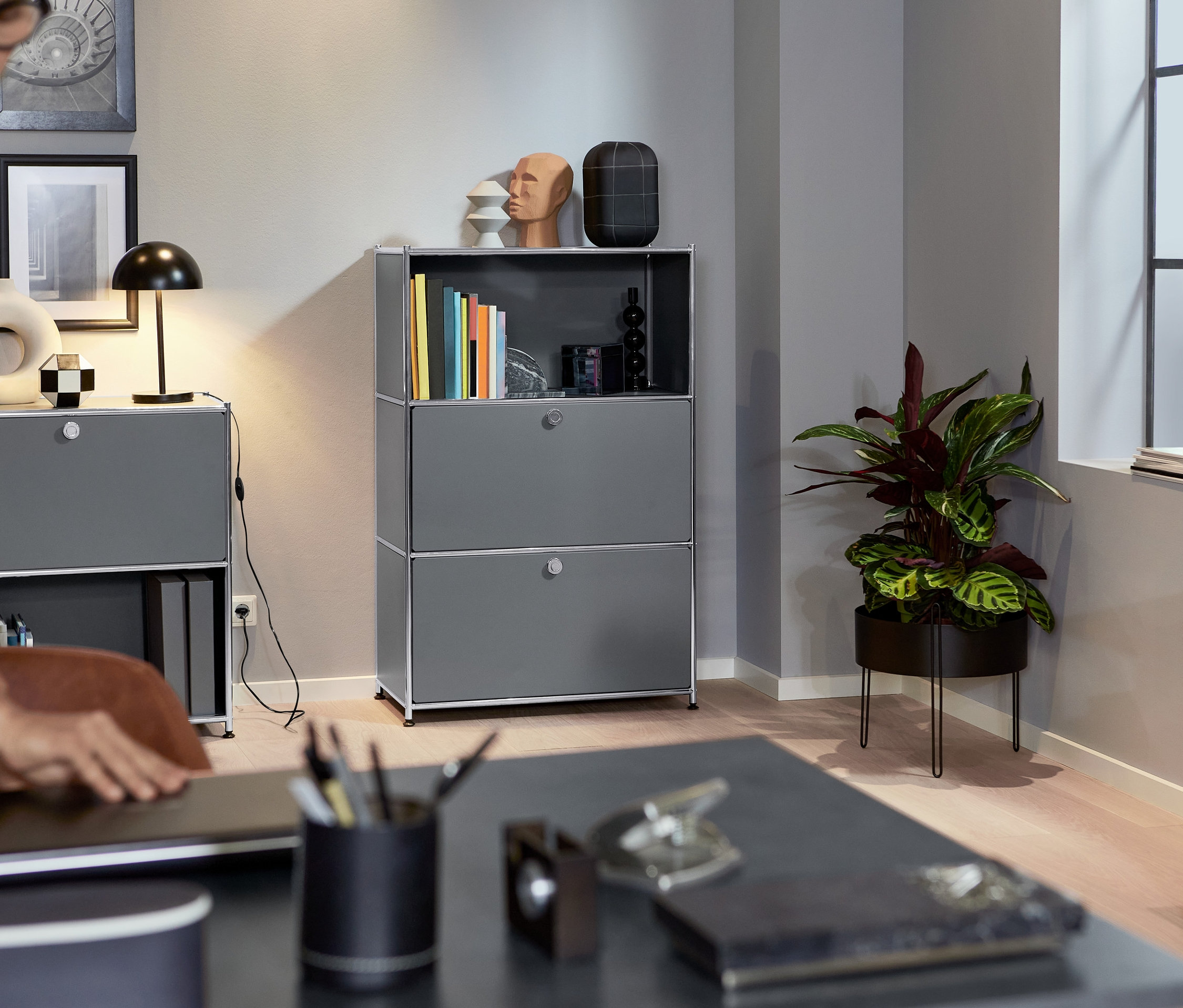 Žena zavírá notebook na stole. V pozadí je kovový regál se dvěma výklopnými dvířky, šedý.