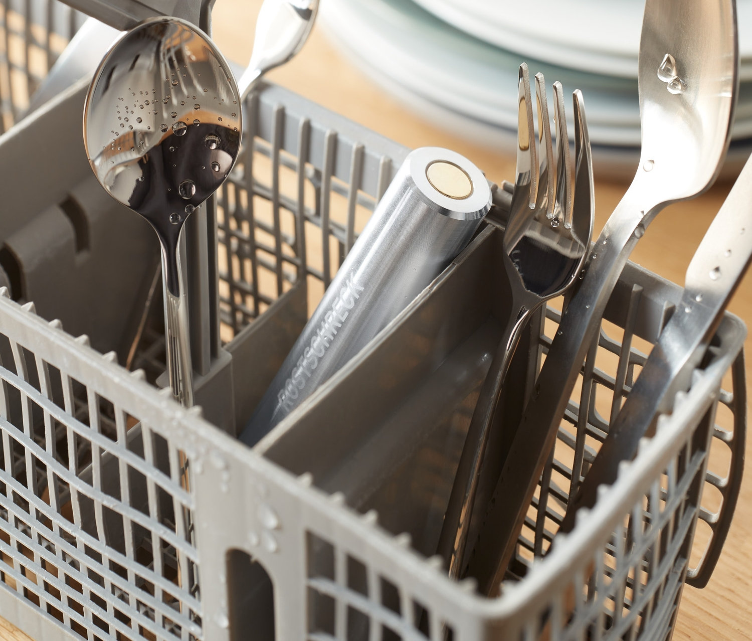 Nerezové příbory v šedém košíku v myčce s Odpuzovač rzi do myčky.