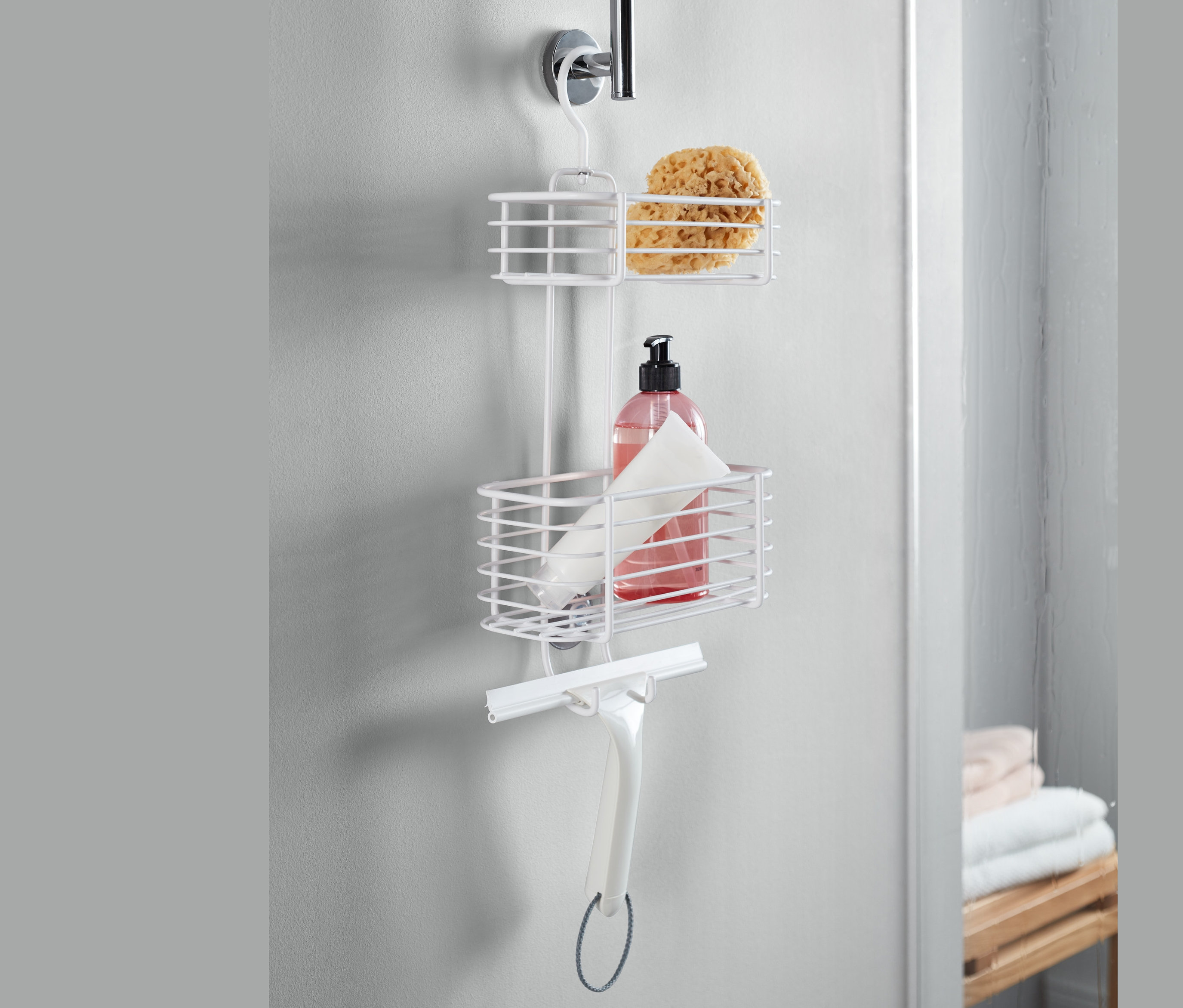 Bílý závěsný regál do sprchy s houbou, lahví a stěrkou.