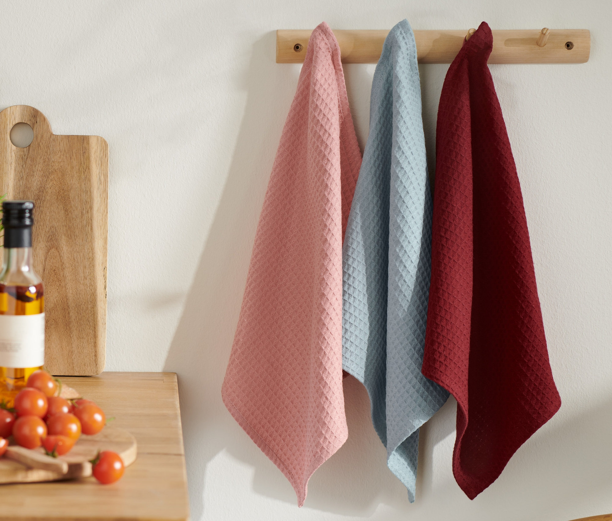 Na dřevěném věšáku visí 3 kuchyňské utěrky.
