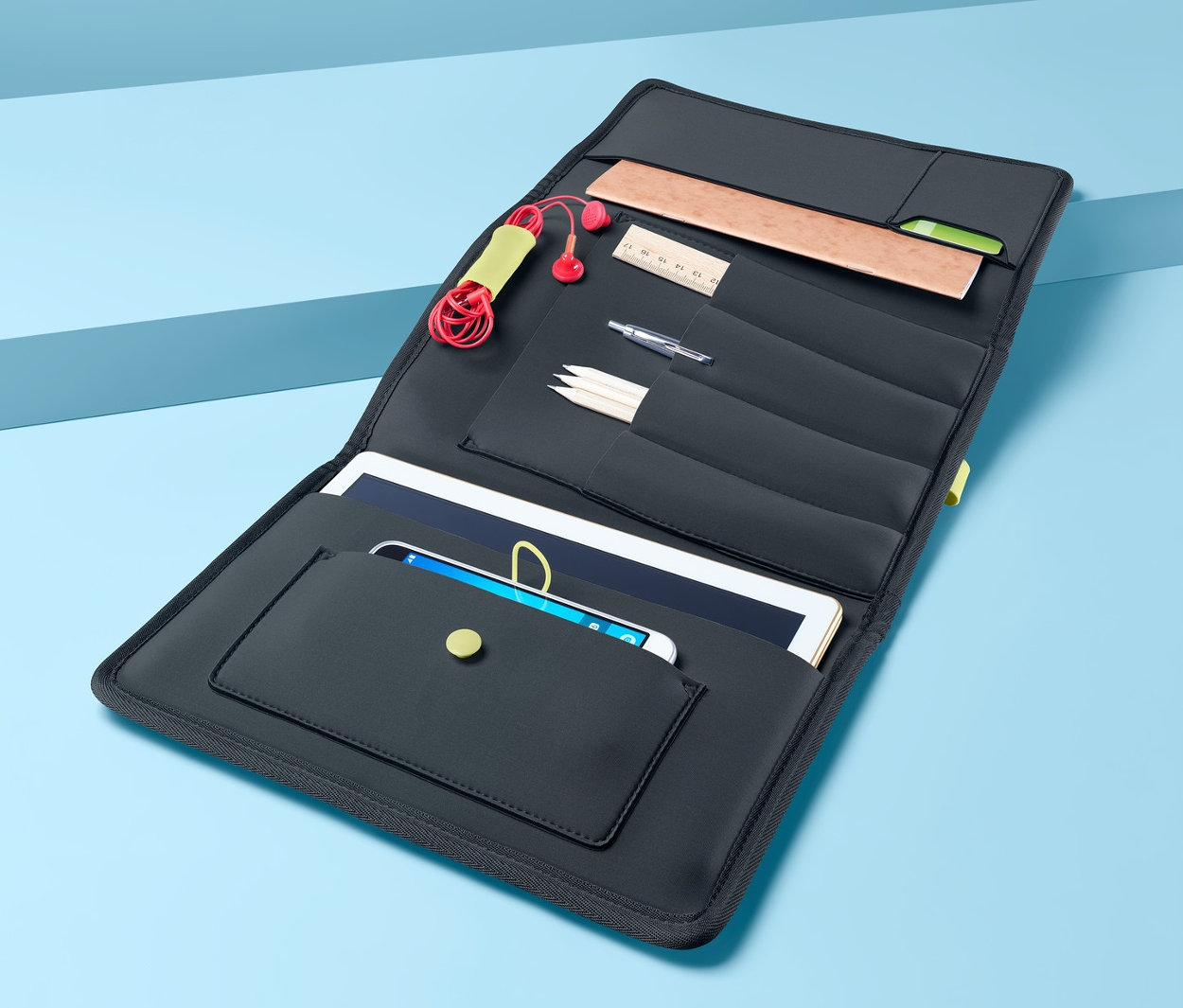 Otevřené desky na kancelářské potřeby s kapsami na tablet, telefon, sluchátka, tužky a pravítko na modrém pozadí.